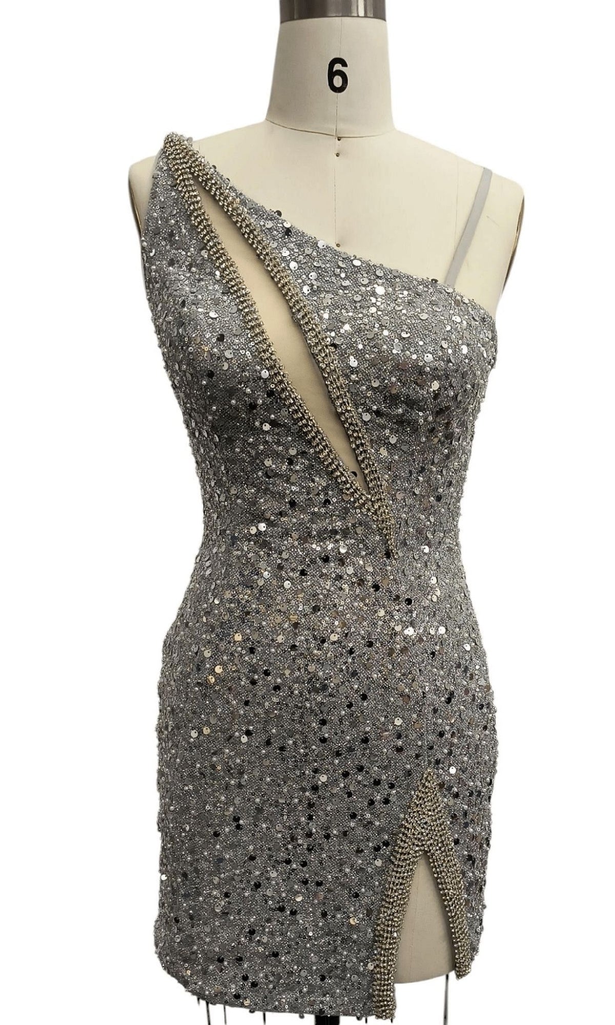 A Short Silver Homecoming Dress (12353) with an asymmetrical neckline and beaded trim, adorned in sequins, is displayed on a dress form labeled with the number 6.